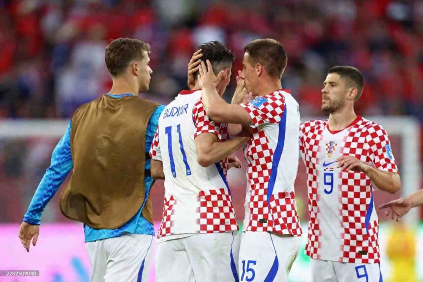 Croatia midfielder Mario Pasalic and forward Andrej Kramaric wearing red and white checkered 9 jersey celebrate by hugging forward Ante Budimir in 11 jersey after a win Fourth Croatia player in checkered jersey visible on right Blurred crowd in red and pink LED advertising board in background during 2026 World Cup Group L match between Panama and Croatia at Toronto Stadium Toronto on June 23 2026  trybalnews