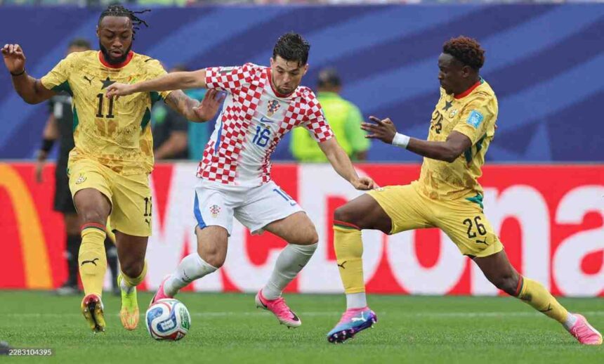 Croatia midfielder Martin Baturina wearing a red and white checkered kit with number 16 controls the ball in the center He is challenged by two Ghana players in yellow kits Marvin Senaya number 11 on the left and Ghana 26 on the right The 2026 FIFA World Cup Group L match between Croatia and Ghana took place on June 27 2026 at Philadelphia Stadium in Philadelphia Pennsylvania Stadium advertising boards and a green pitch are visible in the background  trybalnews