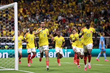 Colombia defender Daniel Muñoz wearing yellow jersey with blue #2 and white shorts celebrates with right index finger raised. Five Colombia teammates in matching yellow jerseys and red socks run alongside him near the goalpost. Crowd in yellow fills the stadium background during FIFA World Cup 2026 Group K match between Colombia and Congo DR at Guadalajara Stadium, Zapopan Mexico on June 23, 2026.