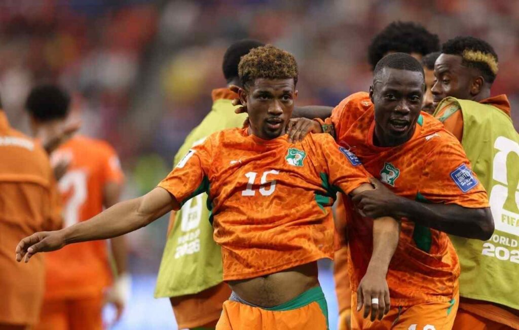 Diallo Trybal News Cote dIvoire midfielder Amad Diallo wearing an orange 15 Puma kit with green accents and curly brown hair celebrates with his mouth open and arm outstretched Teammates in matching orange kits including 20 surround him with big smiles after scoring Cote dIvoires first goal This is during the FIFA World Cup 2026 Round of 32 match between Cote dIvoire and Norway on June 30 2026 at Dallas Stadium in Arlington Texas The background shows a blurred crowd and a player in a green training bib trybalnews
