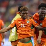 Cote dIvoire midfielder Amad Diallo wearing an orange 15 Puma kit with green accents and curly brown hair celebrates with his mouth open and arm outstretched Teammates in matching orange kits including 20 surround him with big smiles after scoring Cote dIvoires first goal This is during the FIFA World Cup 2026 Round of 32 match between Cote dIvoire and Norway on June 30 2026 at Dallas Stadium in Arlington Texas The background shows a blurred crowd and a player in a green training bib  trybalnews