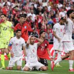 IR Iran players in white kits with red numbers show frustration after a missed chance Player 4 kneels on the grass with both hands on his head while teammate 5 kneels beside him with a shocked expression Teammate 11 stands to the right pointing and shouting Egypt goalkeeper 23 in a neon yellow kit and defender 21 in red watch on 2026 FIFA World Cup Group G match between Egypt and IR Iran on June 26 2026 at Seattle Stadium in Seattle Washington A red Coca Cola hoarding and packed crowd in red and white are in the background  trybalnews