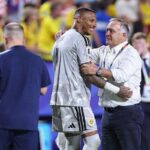 Curaçao goalkeeper Eloy Room wearing a light grey goalkeeper jersey with number 1 and white shorts embraces Dick Advocaat the Curaçao manager and head coach Room smiles toward the right while Advocaat wearing a white button down shirt dark trousers and a FIFA World Cup accreditation lanyard has his left arm around Rooms shoulder and his right hand on Rooms arm Both appear to be sharing a positive moment at full time The background is blurred with stadium seats and fans wearing yellow Match was FIFA World Cup 2026 Group E Ecuador vs Curaçao at Kansas City Stadium Kansas City Missouri United States on June 20 2026  trybalnews