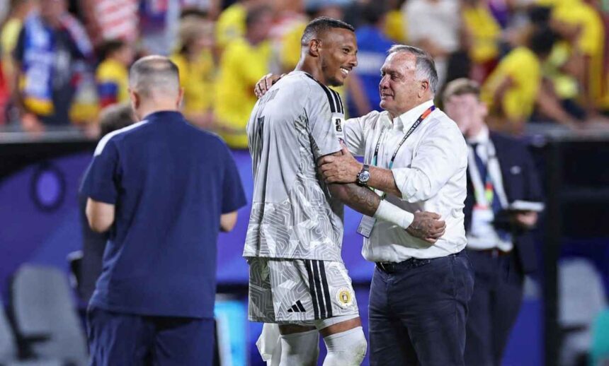 Curaçao goalkeeper Eloy Room wearing a light grey goalkeeper jersey with number 1 and white shorts embraces Dick Advocaat the Curaçao manager and head coach Room smiles toward the right while Advocaat wearing a white button down shirt dark trousers and a FIFA World Cup accreditation lanyard has his left arm around Rooms shoulder and his right hand on Rooms arm Both appear to be sharing a positive moment at full time The background is blurred with stadium seats and fans wearing yellow Match was FIFA World Cup 2026 Group E Ecuador vs Curaçao at Kansas City Stadium Kansas City Missouri United States on June 20 2026  trybalnews