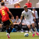 Soccer player in white number 8 dribbling the ball toward the goal while guarded by a opponent in red jersey on a sunny field  trybalnews