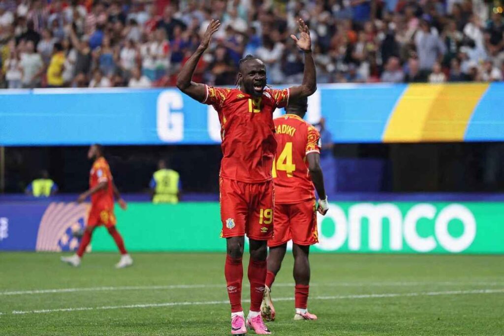 Fiston Mayele Trybal News Congo DR forward Fiston Mayele wearing a red and yellow kit with number 19 and pink boots celebrates with both arms raised and mouth open after his teams third goal Teammate 4 with aposDIADIKIapos on the back of his red kit stands beside him The 2026 FIFA World Cup Group K match between DR Congo and Uzbekistan took place on June 27 2026 at Atlanta Stadium in Atlanta Georgia A packed stadium crowd and blue and yellow advertising boards are visible in the background trybalnews
