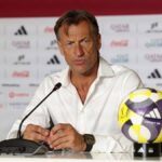 Man in a white shirt sits at a press conference microphone in front with water bottles and a colorful soccer ball on the table  trybalnews