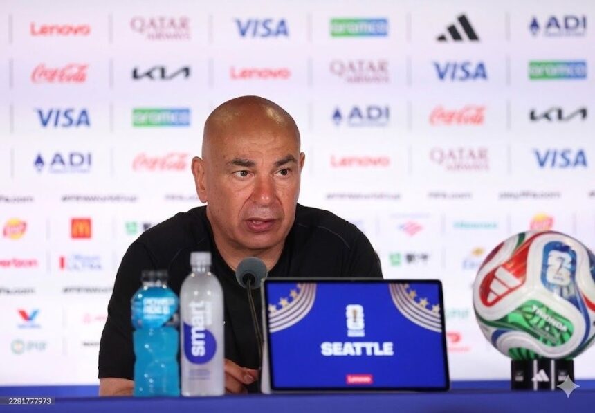 Man at a sports press conference with a Seattle laptop water bottles and a soccer ball on the table behind him  trybalnews