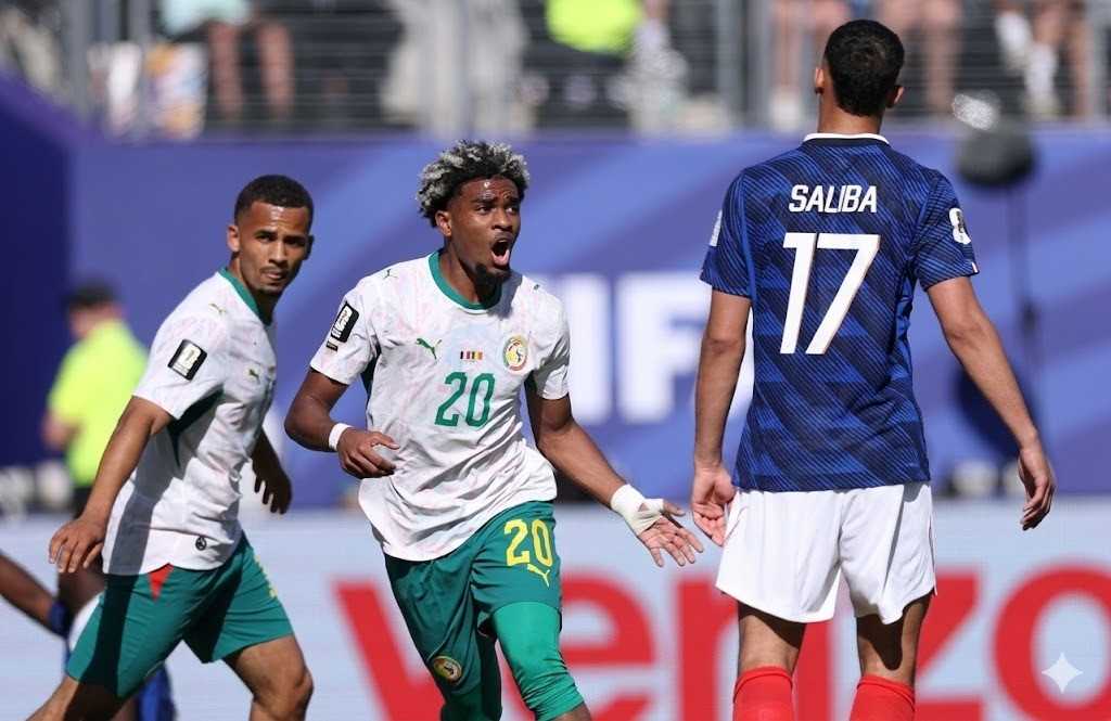 IbrahimMbaye Trybal News Two football players on the field Ibrahim Mbaye of Senegal in white and green number 20 celebrating with mouth open while a teammate in white and green watches nearby on the left A third player in a blue jersey with the name Saliba and number 17 stands with his back to the camera on the right during a match trybalnews