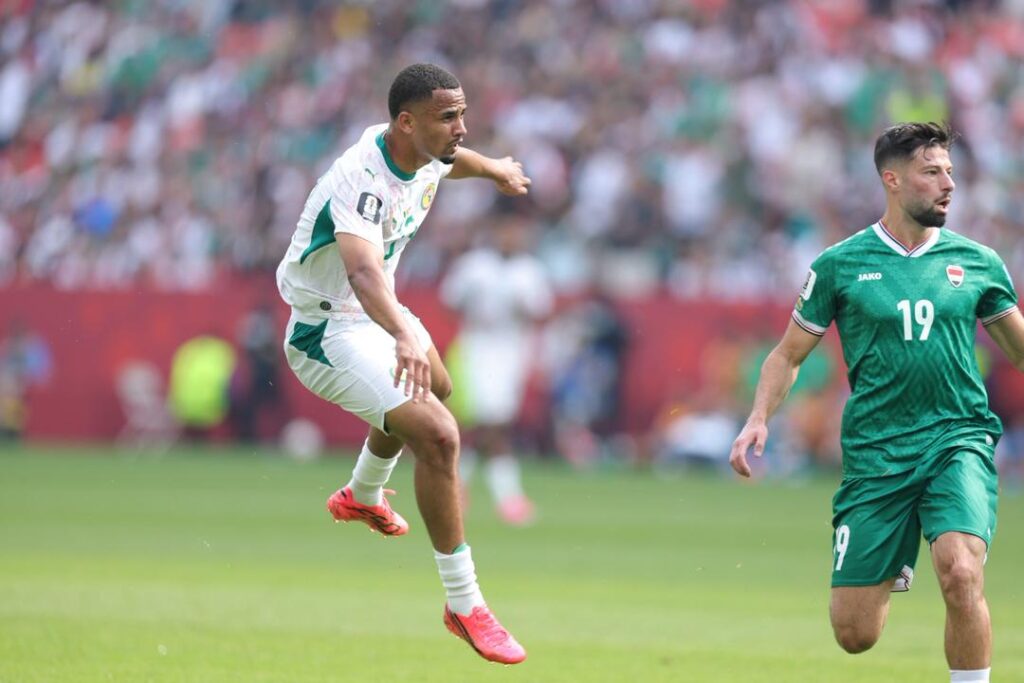 Iliman Ndiaye Trybal News Senegal forward Iliman Ndiaye 13 in a white away kit with green side panels and bright pink cleats is airborne leaping to shoot the ball Iraq defender 19 in a green home kit with white number 19 runs in close pursuit on the right 2026 FIFA World Cup First Stage Group I match between Senegal and Iraq on June 26 2026 at Toronto Stadium also known as BMO Field in Toronto Ontario Canada A blurred crowd in the stands and red advertising hoarding are in the background trybalnews