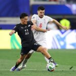 Two soccer players compete for the ball during a match one in black kit number 11 shielding the ball from a white kit opponent number 6  trybalnews