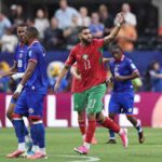 Morocco midfielder Ismael Saibari wearing red 11 jersey with green trim and green shorts celebrates with right arm raised He has a beard short hair white wristband and pink Nike boots with red socks Haiti players in blue kits with 18 visible stand nearby on the pitch Blurred maroon advertising board with white text and stadium crowd in background during FIFA World Cup 2026 Group C match between Morocco and Haiti at Atlanta Stadium Atlanta Georgia on June 24 2026  trybalnews
