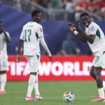 Ismaila Sarr in Senegals white 18 jersey with green trim claps both hands together and shouts in celebration on the pitch A football sits on the grass near his pink and black boots Behind him PM Saar 17 in a white long sleeve jersey looks over his shoulder and teammate 15 covers his mouth with his hand The match is Norway vs Senegal at New York New Jersey Stadium FIFA World Cup 2026 Group I June 22 2026 East Rutherford New Jersey A red FIFA WORLD CUP advertising board is visible behind them  trybalnews