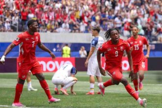 Switzerland forward Johan Manzambi celebrates after scoring his team's first goal during the FIFA World Cup 2026 Group B match between Switzerland and Bosnia and Herzegovina at Los Angeles Stadium in Inglewood, California on June 18, 2026. Manzambi wears a red Switzerland kit with white socks and pink boots, arms outstretched as he runs.