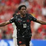 Jonathan David of Canada celebrates after scoring Canadas second goal vs Qatar at FIFA World Cup 2026 BC Place Vancouver June 18 2026 He wears a black Canada kit 10 with arms spread wide crowd blurred red behind him  trybalnews