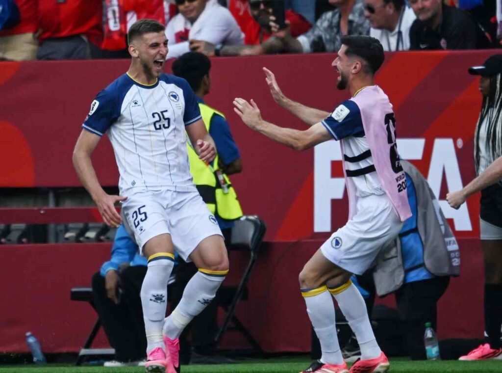 JovoLukic Trybal News Two football players in white uniforms for Bosnia celebrate on the sideline after scoring against Canada at FIFA World Cup Opener one wearing number 25 with pink cleats the other approaching with arms raised trybalnews