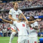 Three England footballers celebrate a goal on the pitch one lifted on his teammates shoulders as others raise their arms in jubilation stadium full of fans behind them in win over Croatia  trybalnews