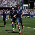 Bosnia and Herzegovina forward Kerim Alajbegovic wearing dark blue 19 jersey with yellow numbers celebrates with arms open while teammate Esmir Bajraktarevic in dark blue 20 jersey runs beside him Teammate 24 celebrates with arms raised in background Players on green pitch with blurred blue and white crowd in packed stadium during FIFA World Cup 2026 Group B match between Bosnia and Herzegovina and Qatar at Seattle Stadium on June 24 2026  trybalnews