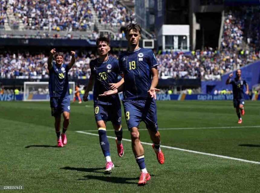 Bosnia and Herzegovina forward Kerim Alajbegovic wearing dark blue 19 jersey with yellow numbers celebrates with arms open while teammate Esmir Bajraktarevic in dark blue 20 jersey runs beside him Teammate 24 celebrates with arms raised in background Players on green pitch with blurred blue and white crowd in packed stadium during FIFA World Cup 2026 Group B match between Bosnia and Herzegovina and Qatar at Seattle Stadium on June 24 2026  trybalnews