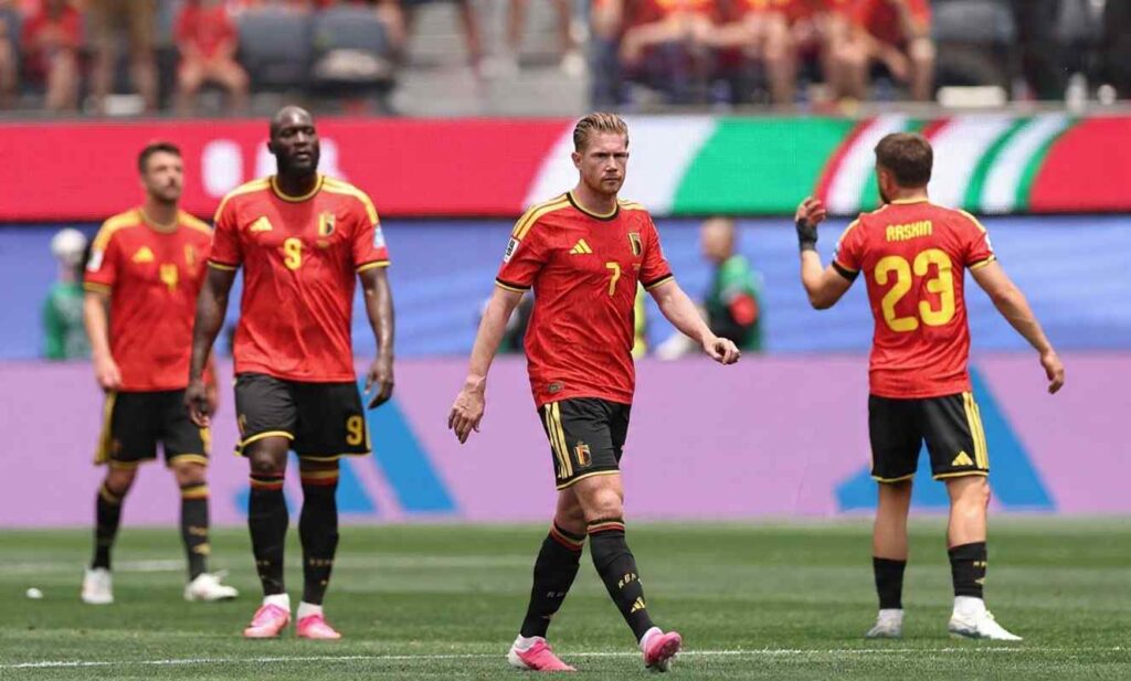 Belgium midfielder Kevin De Bruyne wearing number 7 red jersey with yellow trim walks on the pitch with hands slightly out and frustrated expression Teammates Romelu Lukaku 9 and others in red jerseys are behind him Stadium crowd and hoardings blurred in background at Los Angeles Stadium June 21 2026 after Iran goal disallowed for offside  trybalnews