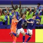 Blue clad Japanese soccer players celebrate a goal on the field as cheering fans fill the stands behind them  trybalnews