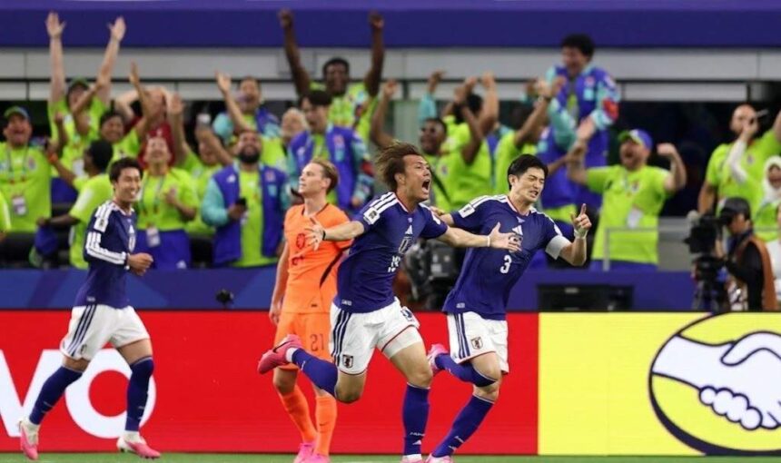 Blue clad Japanese soccer players celebrate a goal on the field as cheering fans fill the stands behind them  trybalnews