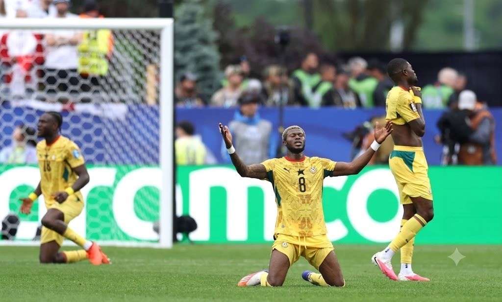 Kwasi Sibo Trybal News Ghana midfielder Kwasi Sibo wearing yellow 8 jersey kneels on the pitch with arms raised in celebration after a scoreless 0 0 draw Two Ghana teammates in yellow jerseys visible behind him near the goalpost during FIFA World Cup 2026 Group L match between England and Ghana at Boston Stadium Foxborough Massachusetts on June 23 2026 Green LED advertising board in background trybalnews