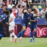 Kylian Mbappé in Frances dark blue 10 jersey runs with both arms raised and index fingers pointing up He has a captains armband on his left arm and wears pink football boots Teammates and an opponent are visible behind him The match is France vs Iraq at Philadelphia Stadium during the FIFA World Cup 2026 Group I June 22 2026 Philadelphia Pennsylvania Crowd and LED boards are blurred in the background  trybalnews