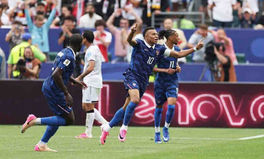 Kylian Mbappé in Frances dark blue 10 jersey runs with both arms raised and index fingers pointing up He has a captains armband on his left arm and wears pink football boots Teammates and an opponent are visible behind him The match is France vs Iraq at Philadelphia Stadium during the FIFA World Cup 2026 Group I June 22 2026 Philadelphia Pennsylvania Crowd and LED boards are blurred in the background  trybalnews