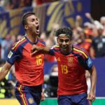 Spain players Lamine Yamal wearing number 19 red jersey with white headband and Rodri wearing number 16 red jersey celebrate on the pitch Yamal has his arm around Rodris shoulder both with mouths open shouting Crowd and blue stadium hoardings are blurred in the background at Atlanta Stadium June 21 2026  trybalnews
