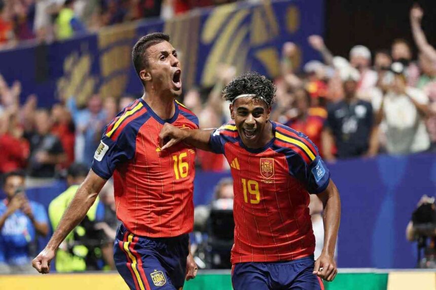 Spain players Lamine Yamal wearing number 19 red jersey with white headband and Rodri wearing number 16 red jersey celebrate on the pitch Yamal has his arm around Rodris shoulder both with mouths open shouting Crowd and blue stadium hoardings are blurred in the background at Atlanta Stadium June 21 2026  trybalnews