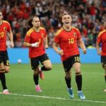 Belgium forward Leandro Trossard wearing a red home kit with yellow shoulder stripes and number 10 celebrates with his mouth open and fists clenched after scoring He runs on the pitch at BC Place with teammates 20 3 with a white wrist bandage and captain 6 with an armband behind him All wear red shirts black shorts with yellow numbers and colorful cleats 2026 FIFA World Cup Group G match between New Zealand and Belgium on June 26 2026 at BC Place in Vancouver British Columbia A blurred crowd in red fills the stadium background  trybalnews