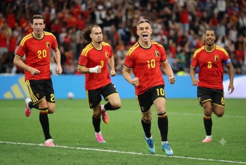 Belgium forward Leandro Trossard wearing a red home kit with yellow shoulder stripes and number 10 celebrates with his mouth open and fists clenched after scoring He runs on the pitch at BC Place with teammates 20 3 with a white wrist bandage and captain 6 with an armband behind him All wear red shirts black shorts with yellow numbers and colorful cleats 2026 FIFA World Cup Group G match between New Zealand and Belgium on June 26 2026 at BC Place in Vancouver British Columbia A blurred crowd in red fills the stadium background  trybalnews