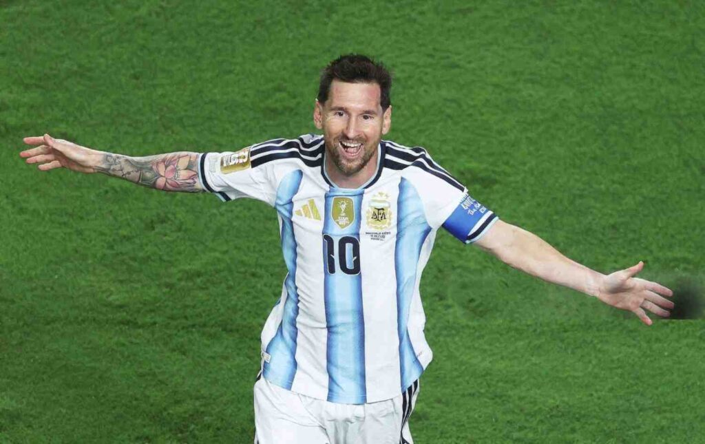 Lionel Messi Trybal News Argentine footballer Lionel Messi in a white and blue jersey with arms outstretched celebrating on a green pitch after scoring a hat trick against Algeria trybalnews