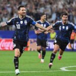 Argentina captain Lionel Messi wearing a dark blue patterned kit with number 10 and a blue captains armband celebrates with both arms outstretched and a smile Teammates in matching dark blue kits run in behind him on the pitch The 2026 FIFA World Cup Group J match between Jordan and Argentina took place on June 27 2026 at Dallas Stadium in Arlington Texas A packed stadium crowd and red and blue advertising boards are blurred in the background  trybalnews