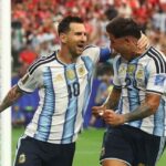 Argentina captain Lionel Messi 10 and teammate Enzo Fernandez 24 celebrate next to the goal post Messi has his arm around Fernandezs head and is shouting with joy Both wear Argentinas light blue and white striped jerseys and navy shorts The goal net is on the left and a blurred crowd fills the stands behind them at Dallas Stadium June 22 2026  trybalnews