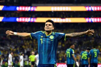 Colombian soccer goalkeeper in a blue kit with arms extended in celebration on the field.