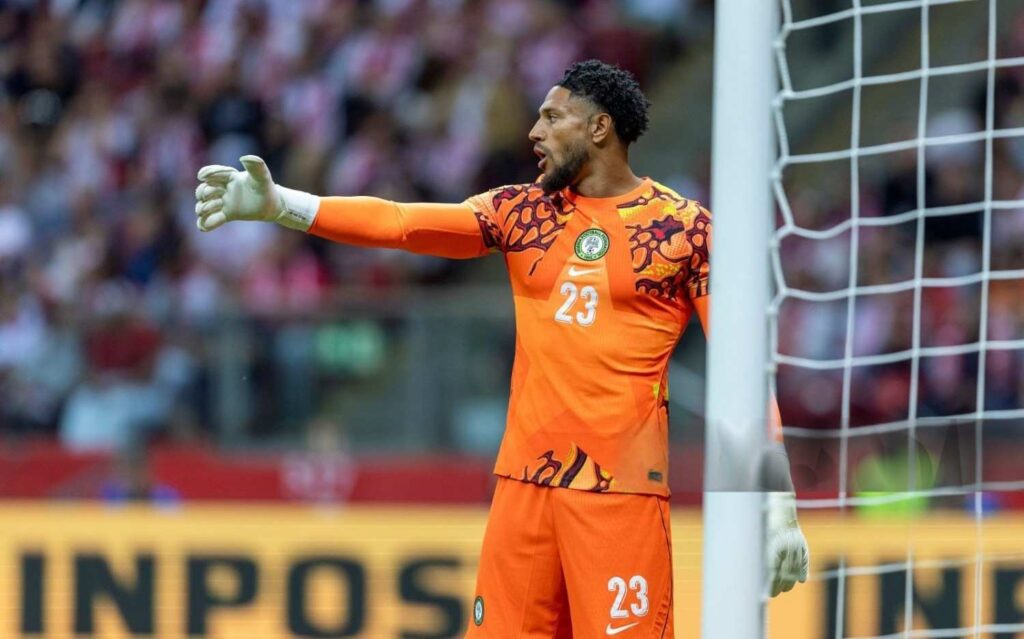 Maduka Okoye Trybal News Nigerian goalkeeper in an orange kit with number 23 gesturing with his left arm near the goal in a stadium crowd behind him trybalnews