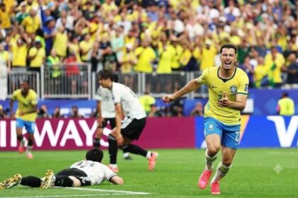 Brazil forward Gabriel Martinelli, wearing a yellow #22 Brazil kit with blue shorts and pink cleats, celebrates after scoring Brazil’s second goal. He is running with arms outstretched and mouth open in celebration on the pitch. Behind him, two Japan players in white kits are dejected, one lying on the grass and another running away. The FIFA World Cup 2026 Round of 32 match between Brazil and Japan took place on June 29, 2026 at Houston Stadium in Houston, Texas. A packed stadium of yellow-clad Brazil fans cheers in the background, with Qatar Airways hoardings visible around the pitch.