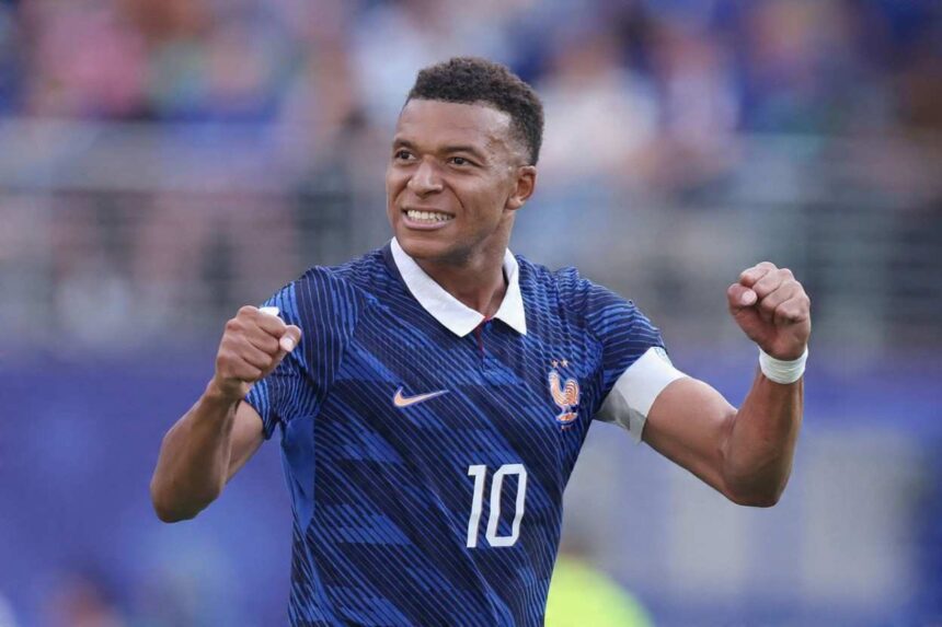 Footballer in a blue France jersey with number 10 celebrates with fists raised smiling on the pitch  trybalnews