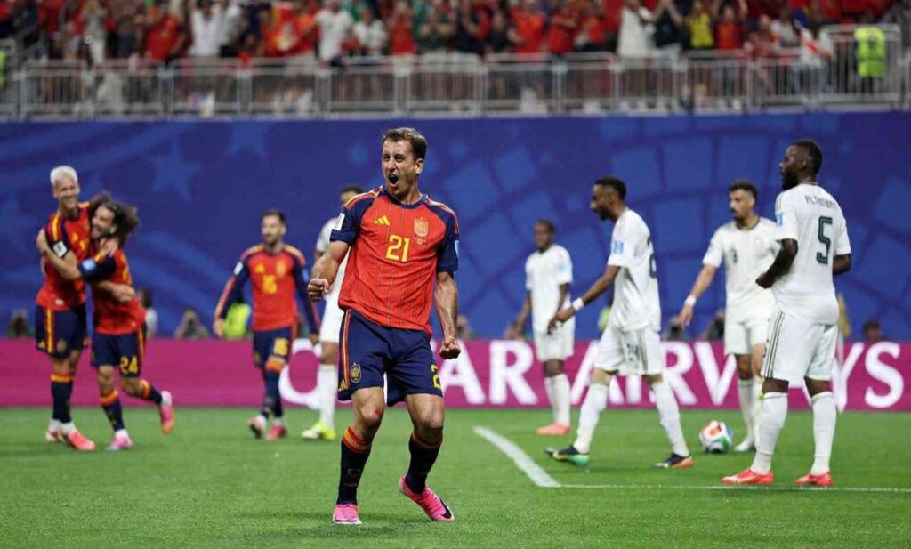 Mikel Oyarzabal Trybal News Spain forward Mikel Oyarzabal wearing number 21 red jersey with yellow trim shouts with clenched fists on the pitch Hes in foreground with mouth open celebrating Behind him Spain teammates hug on left side and Saudi Arabia players in white jerseys walk away Crowd in red fills the stands at Atlanta Stadium June 21 2026 trybalnews