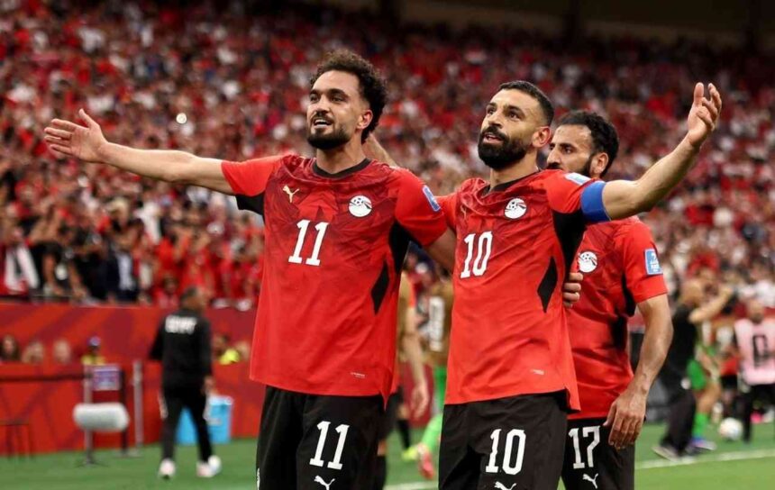 Egypt footballers Mohamed Salah wearing 10 and Mostafa Zico wearing 11 celebrate a goal Both in red Egypt jerseys with black shorts arms spread wide smiling in front of a packed red crowd at BC Place Vancouver during the FIFA World Cup 2026 Group G match vs New Zealand on June 21 2026  trybalnews