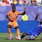 Cote dIvoire forward Nicolas Pepe wearing orange 19 Puma jersey orange shorts orange socks and pink football boots controls the ball on the pitch He is leaning forward with his right arm slightly out for balance as a Curacao defender in blue 5 kit slides on the ground beside him The match ball is airborne to Pepes left FIFA World Cup 2026 Group E match between Curacao and Cote dIvoire at Philadelphia Stadium Philadelphia Pennsylvania on June 25 2026 Cote dIvoire crest and Puma logo visible on kit  trybalnews