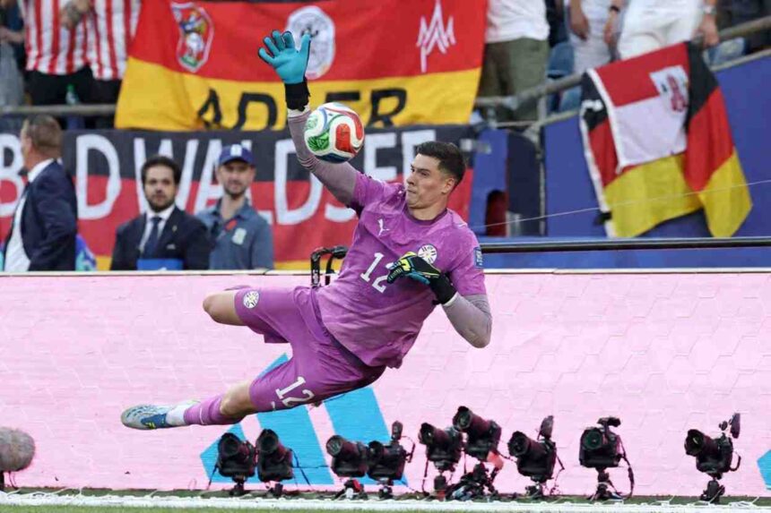 Goalkeeper in a purple kit dives to punch away a high ball during a match with flags and fans in the background  trybalnews