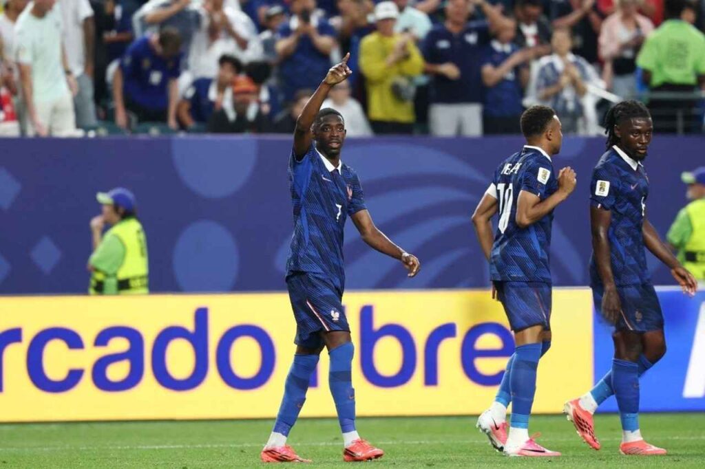 Ousmane Dembele in Frances dark blue 7 jersey points his right index finger upward with his left arm extended He wears blue shorts socks and red football boots Behind him Kylian Mbappé 10 jogs with his right fist raised and Marcus Thuram 9 walks beside him The match is France vs Iraq at Philadelphia Stadium during the FIFA World Cup 2026 Group I June 22 2026 Philadelphia Pennsylvania Fans in blue jerseys and a yellow LED advertising board are blurred in the background  trybalnews