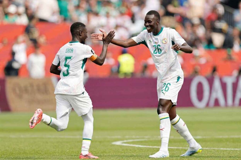 Pape Gueye Trybal News Senegal midfielder Pape Gueye 26 in a white away kit with green trim and number 26 smiles and high fives captain Idrissa Gana Gueye 5 who wears the same kit with GANA and number 5 on the back and an orange armband Both players are on the pitch celebrating 2026 FIFA World Cup Group I match between Senegal and Iraq on June 26 2026 at Toronto Stadium in Toronto Ontario Red stadium seats and blurred fans in the background trybalnews