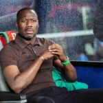 Senegal coach Pape Thiaw sits on a grey bench in the dugout wearing a brown polo shirt black trousers silver bracelet and green watch He has his hands clasped and looks intently downfield with a serious expression Raindrops are visible on the glass in front of him A colorful towel is draped over the seat behind him and a green jacket is next to him The scene is before the FIFA World Cup 2026 Group I match between Norway and Senegal at New York New Jersey Stadium East Rutherford New Jersey June 22 2026  trybalnews