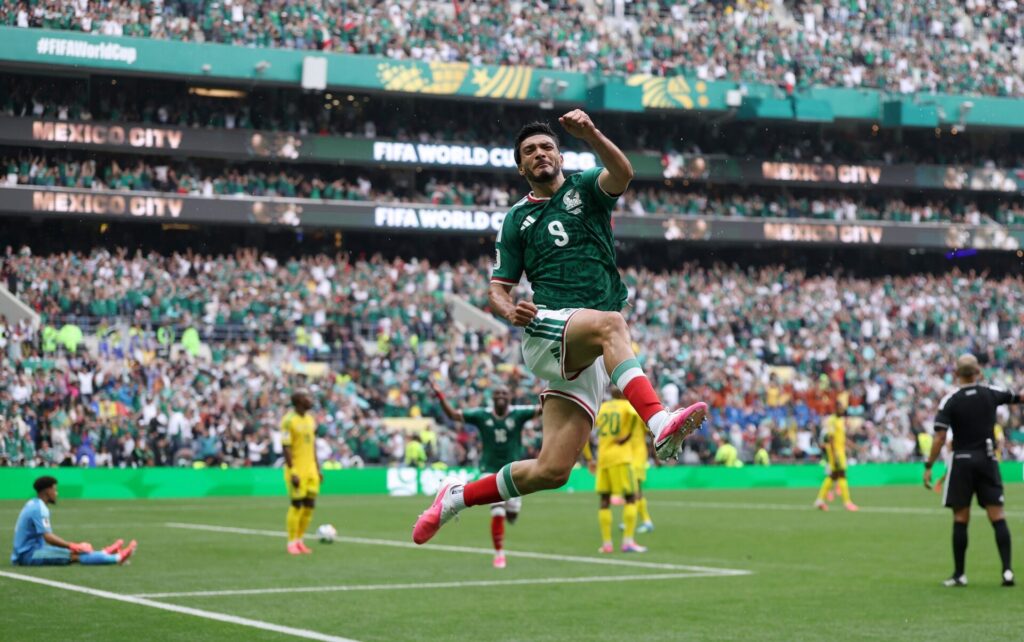 Raul Jimenez Trybal News Soccer player in a green Mexico jersey number 9 leaps midair as fans cheer in a packed stadium trybalnews