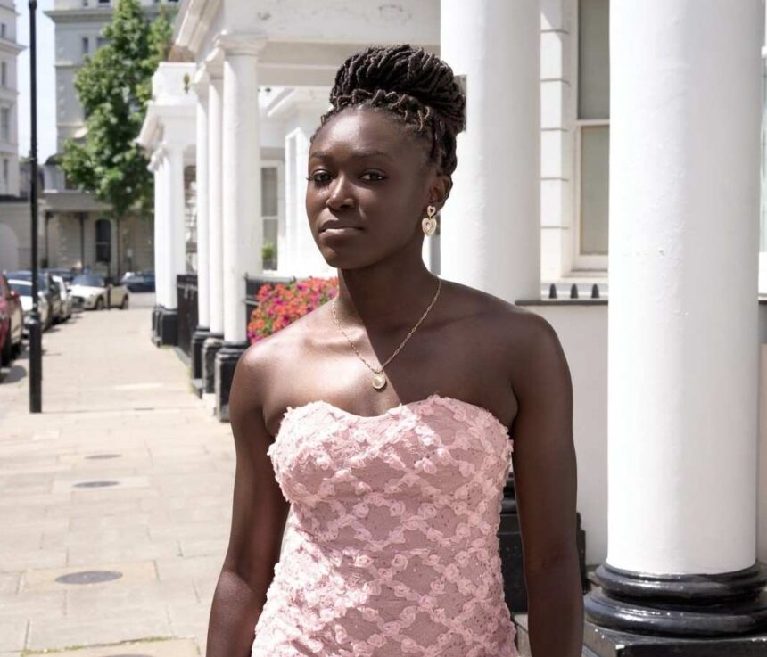 Young woman with braided hair in a pink strapless lace dress standing on a sunlit city sidewalk by white columns and a row of buildings  trybalnews