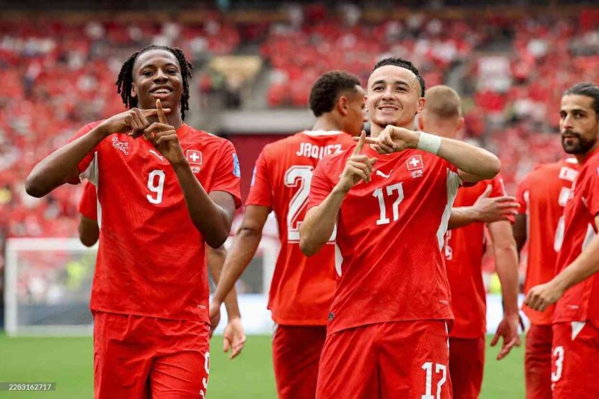 Switzerland forward Ruben Vargas wearing red 17 jersey and teammate Johan Manzambi in red 9 jersey celebrate with hand gestures forming a triangle Both players smile on the pitch with blurred red crowd and green grass in background during FIFA World Cup 2026 Group B match between Switzerland and Canada at BC Place Vancouver on June 24 2026 Switzerland defender Jaquez 2 visible behind them  trybalnews